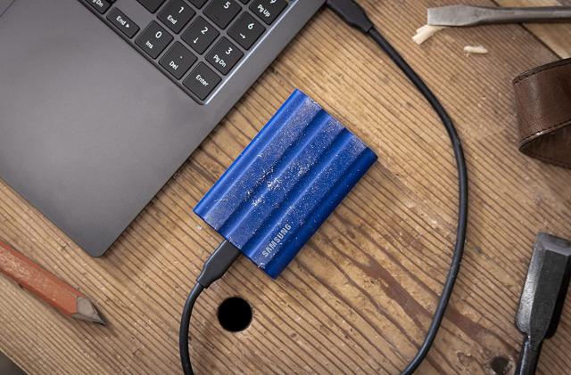 A photo of a Samsung T7 Shield Portable SSD plugged into a laptop on a table.