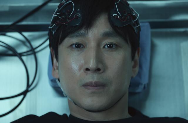 A still from Apple TV+ series Dr. Brain in which Sewon (Lee Sun-kyun) lies on a table wearing a headpiece covered in wires.