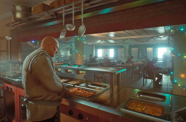 A cook works behind the counter of a cafeteria with hotplates of food ready to serve.