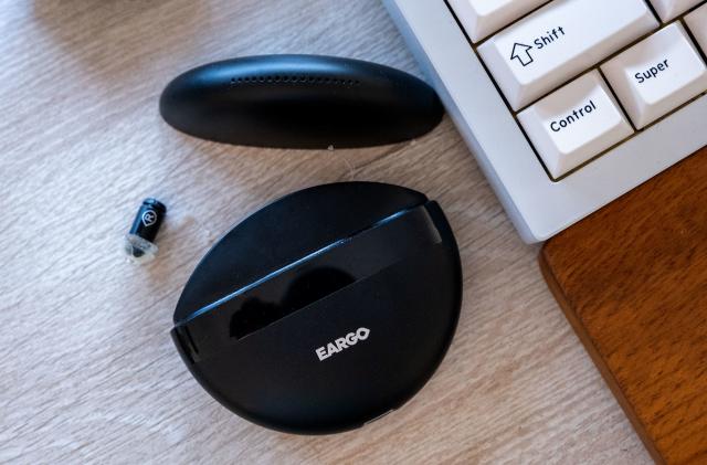 The Eargo hearing aids charging case is pictured open alongside one of the buds.