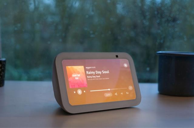 Amazon's Echo Show 5 smart display rests on a tablet in front of a rainy window.