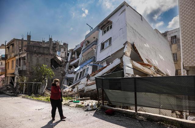 A pedestrian uses a smartphone as she walks past a collapsed building in Antakya, southern Turkey on February 21, 2023. - A 6.4-magnitude earthquake late February 20, rocked Turkey's southern province of Hatay and northern Syria, killing six people and sparking fresh panic after a massive February 6 tremor left nearly 45,000 dead in both countries. (Photo by Sameer Al-DOUMY / AFP) (Photo by SAMEER AL-DOUMY/AFP via Getty Images)