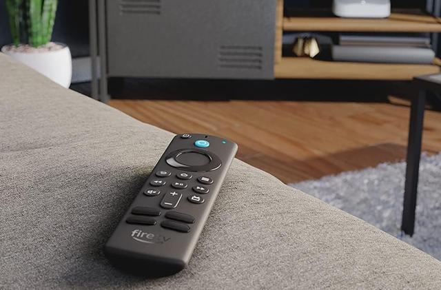 The remote for Amazon's Fire TV stick sits on a couch, pointed towards an entertainment center. 