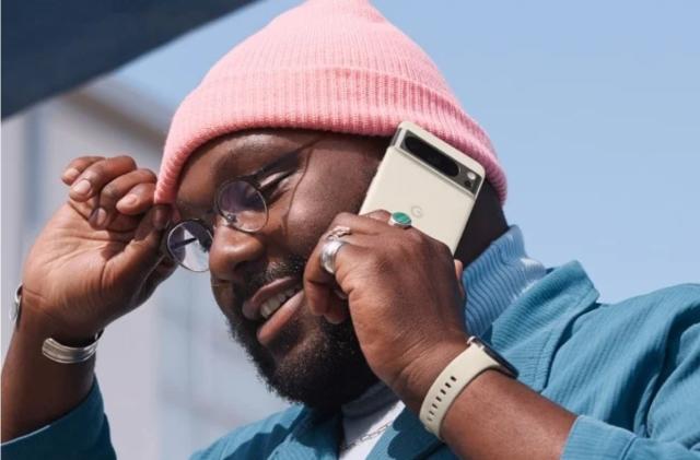 A man wearing a pink beanie and a blue blazer holding a porcelain-colored smartphone against his ear.