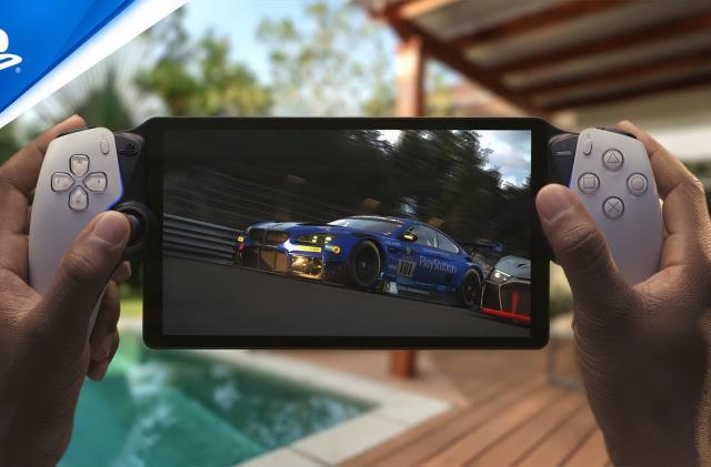 Marketing photo of the Sony PlayStation Portal remote play handheld. A person’s hands grip the portable console with a racing sim on the screen. In the background is a luxurious pool and deck with lawn chairs.