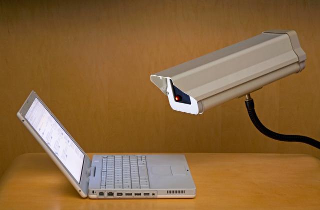 A surveillance camera is peering into the screen of a laptop computer.