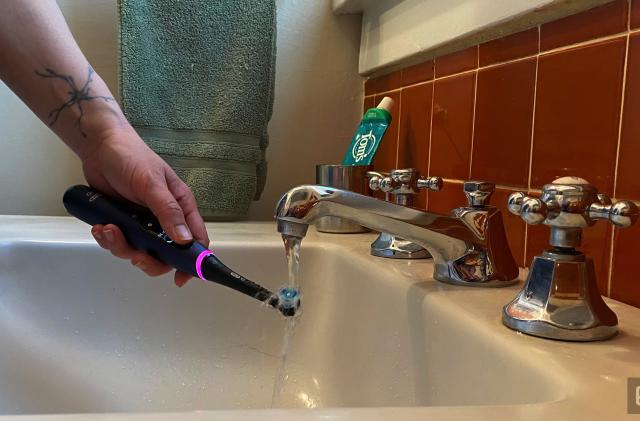 The Oral-B series 7 smart toothbrush under running water in a bathroom sink. 
