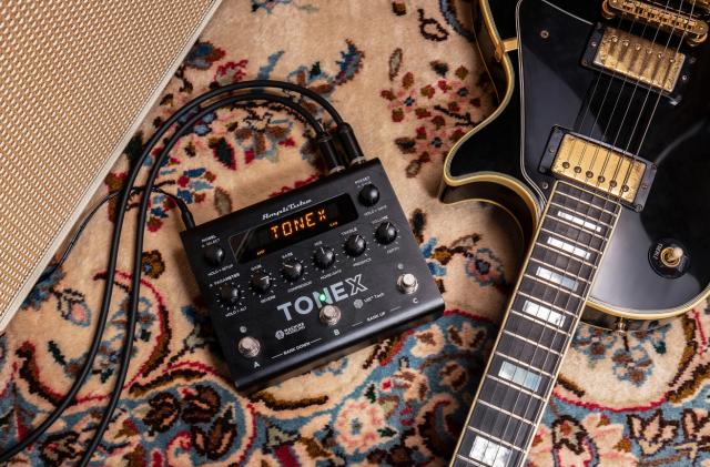 An IK Multimedia ToneX Pedal on very pretty rug next to a black and gold Les Paul. 